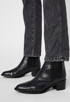 Schwarze, strukturierte Leder-Stiefeletten mit spitzen Zehen und niedrigen Blockabsätzen, getragen zu dunkelgrauen Denim-Jeans.