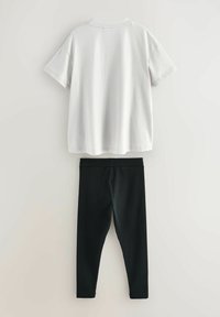 Bijela kratka majica s okruglim izrezom preko crnih rastezljivih tajica, oba izrađena od mekanog tkanja, prikazana na neutralnoj pozadini.