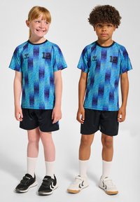 Ungdomsfotbollströjor i blått med ett gradientmönster av mörka till ljusa nyanser. Båda har på sig svarta shorts och olika färgade sportskor.