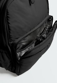 Black insulated backpack pocket unzipped, showing metallic thermal lining and internal mesh zipper compartment.