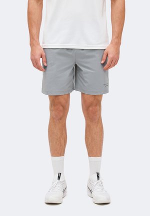 Άνδρας που φοράει ανοιχτό γκρι αθλητικές σορτς, λευκές αθλητικές κάλτσες και λευκά παπούτσια για τρέξιμο σε απλό φόντο.