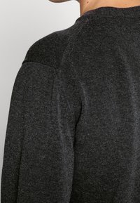 Pull en maille gris foncé avec un col rond et un tissu texturé. Coutures d'épaule visibles et finition lisse.