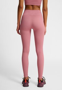 Roze geribde leggings met een hoge tailleband, een getailleerd ontwerp en een gladde textuur, gecombineerd met zwarte en rode sportschoenen.