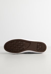 Białe sneakersy z teksturowaną brązową gumową podeszwą, z wzorem bieżnika w kształcie diamentu. Cholewka ma minimalne zdobienia i bezszwowy design.