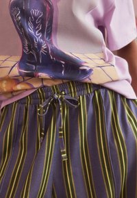 Graphic t-shirt featuring a purple illustration of cowboy boots, paired with striped, drawstring pants in shades of purple and green.