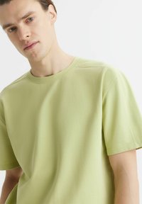 Koszulka typu crew neck z krótkim rękawem w jasnym zielonym kolorze z bawełny. Posiada luźny krój, minimalne detale szwów i gładką teksturę.