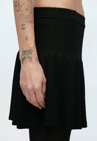 Čierna rebrovaná pletená sukňa so zvonovým lemom. Pás je priliehavý a textúra látky pôsobí mäkko a pružne.