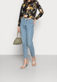 Haut à manches longues noir à motifs floraux avec des fleurs jaunes et roses, jean taille haute bleu clair, sac à main vert et sandales à talons hauts bleu clair.