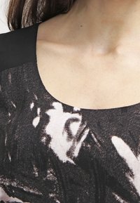 Zbliżenie na górną część klatki piersiowej i szyję osoby noszącej czarno-biały top w wzory z okrągłym dekoltem.