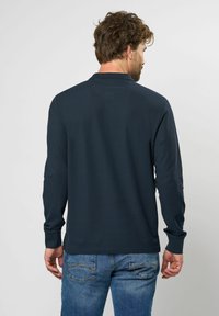 Langærmet marineblå skjorte lavet af glat stof med en ribbet tekstur, med en klassisk krave og manchetter, parret med blå denim jeans.
