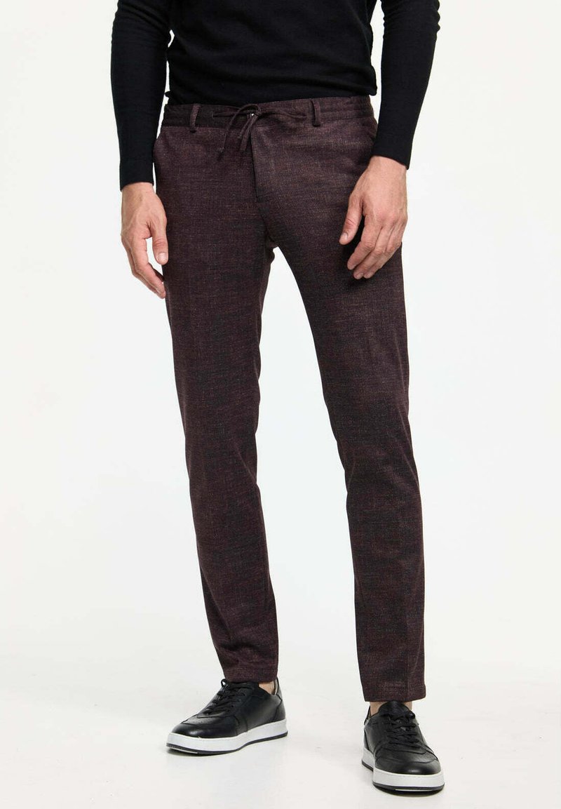 Dunkelburgunderfarbene Hose mit strukturiertem Finish, ausgestattet mit einem elastischen Bund und Kordelzug, kombiniert mit schwarzen Sneakers für Kontrast.