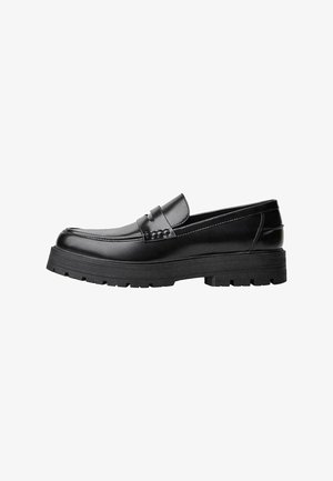 Zwarte leren loafer met een chunky profielzool en een decoratieve band over de bovenkant, weergegeven in het linkerzijprofiel op een witte achtergrond.