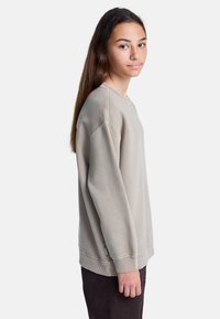 Beige sweatshirt met lange mouwen, ronde halslijn en geribde manchetten. Zachte textuur en casual pasvorm, gedragen met donkere broek.