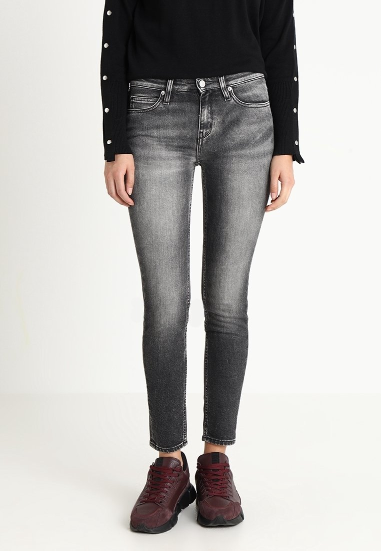 Slim-fit black jeans with a faded wash, five pockets, and contrast stitching, paired with burgundy sneakers and a black sweater.