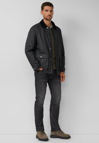 Schwarze leichte Jacke mit Kragen, ausgestattet mit Druckknöpfen und zwei vorderen Taschen. Kombiniert mit dunklen Jeans und braunen Stiefeln.