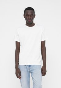 White cotton t-shirt with a round neckline and short sleeves, paired with light blue denim jeans. Simple design, no visible patterns or accents.