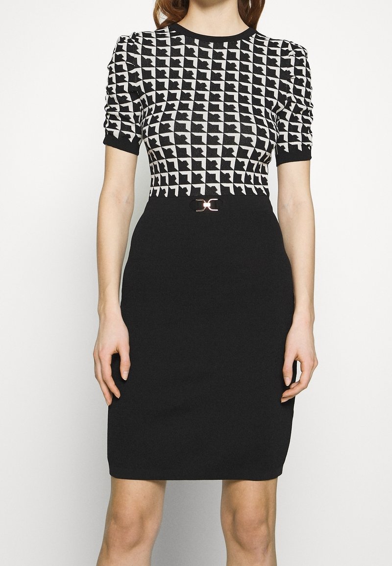 Femme portant un haut à manches courtes à motif pied-de-poule noir et blanc avec une jupe noire taille haute unie dotée d'une petite boucle de ceinture.