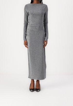Langes silbernes Glitzerkleid mit langen Ärmeln, rundem Ausschnitt und taillierter Silhouette, kombiniert mit schwarzen High Heels.