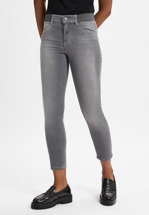 Graue Stretchjeans mit schmaler Passform, fünf Taschen und verkürzter Länge. Kombiniert mit schwarzen Mokassins mit einer klobigen Sohle.