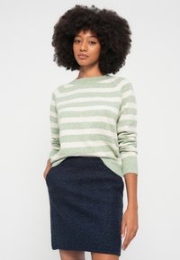 Suéter a rayas verdes y blancas con escote redondo, combinado con una minifalda texturizada de color azul marino oscuro. Tejido suave y ajuste relajado.