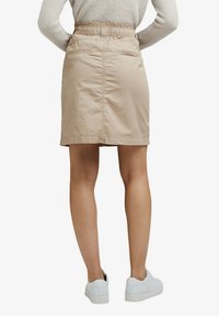 Jupe beige, longueur genoux, avec une taille élastique et des poches latérales. Fabriquée en tissu léger avec une texture lisse. Assortie à des baskets blanches.
