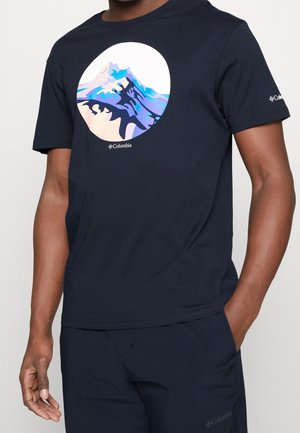 Homme portant un t-shirt Columbia bleu marine avec un motif circulaire de montagne en nuances de bleu et violet sur la poitrine et un pantalon bleu marine assorti.