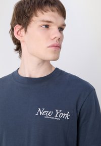 Marineblauwe katoenen t-shirt met een ronde hals, voorzien van witte geborduurde tekst "New York" en "Calvin Klein Jeans" op de linkerkant van de borst.