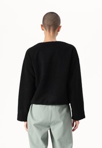 Maglione nero oversize realizzato in tessuto testurizzato, con maniche lunghe e scollatura rotonda, abbinato a pantaloni verde chiaro.