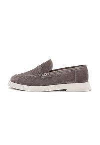 Mocasines de ante gris con una suela de goma blanca ligeramente elevada, que presentan un diseño cosido y un pequeño acento decorativo en la parte superior.