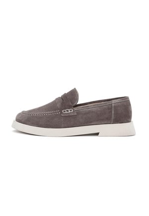 Mocassins en daim gris avec une semelle en caoutchouc blanc légèrement surélevée, présentant un motif cousu et un petit accent décoratif sur le dessus.