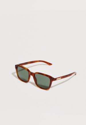 Lunettes de soleil rectangulaires en écaille de tortue marron avec des verres vert foncé et des branches fines posées sur une surface blanche.