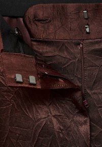Interior din material bordeaux cu o textură ridată, având un fermoar metalic și două accente mici negre din metal pe talie.