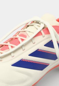 Sport schoen met een voornamelijk witte bovenkant, voorzien van roze en blauwe accenten, ingewikkelde textuur details en witte veters.