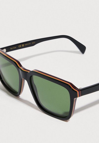 Ochelari de soare negri cu lentile verzi, cu ramă geometrică și un accent în dungi multicolore pe marginea superioară a lentilelor.