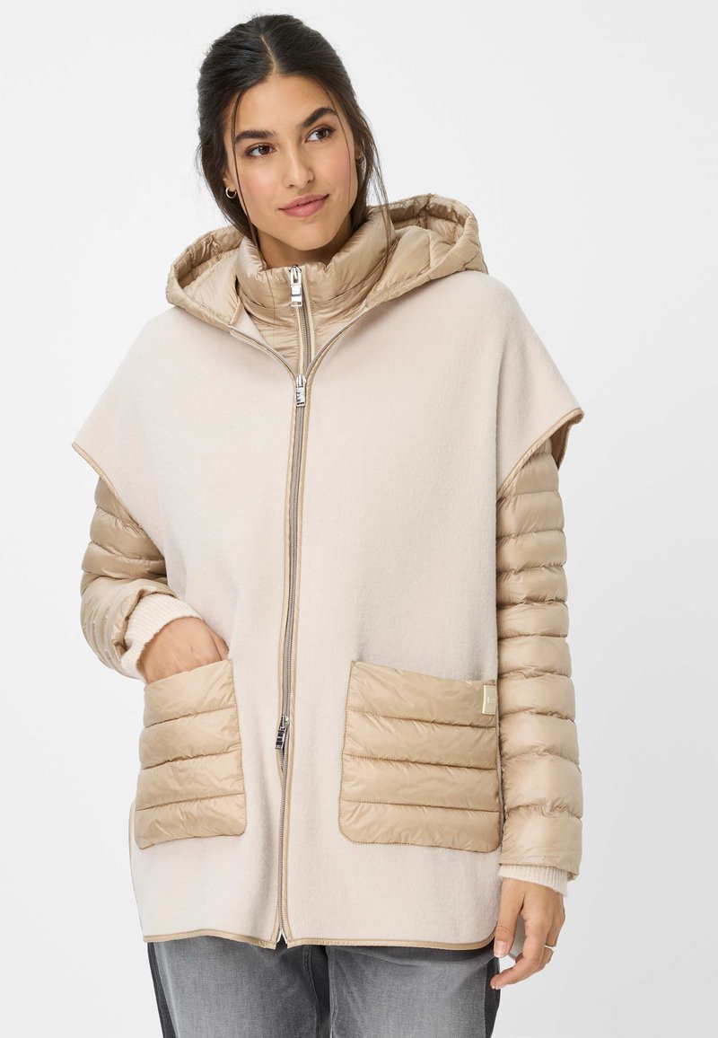 Beige hoodie met een zachte, fleece-achtige body en gewatteerde mouwen. Voorzien van twee zakken aan de voorkant en een ritssluiting.