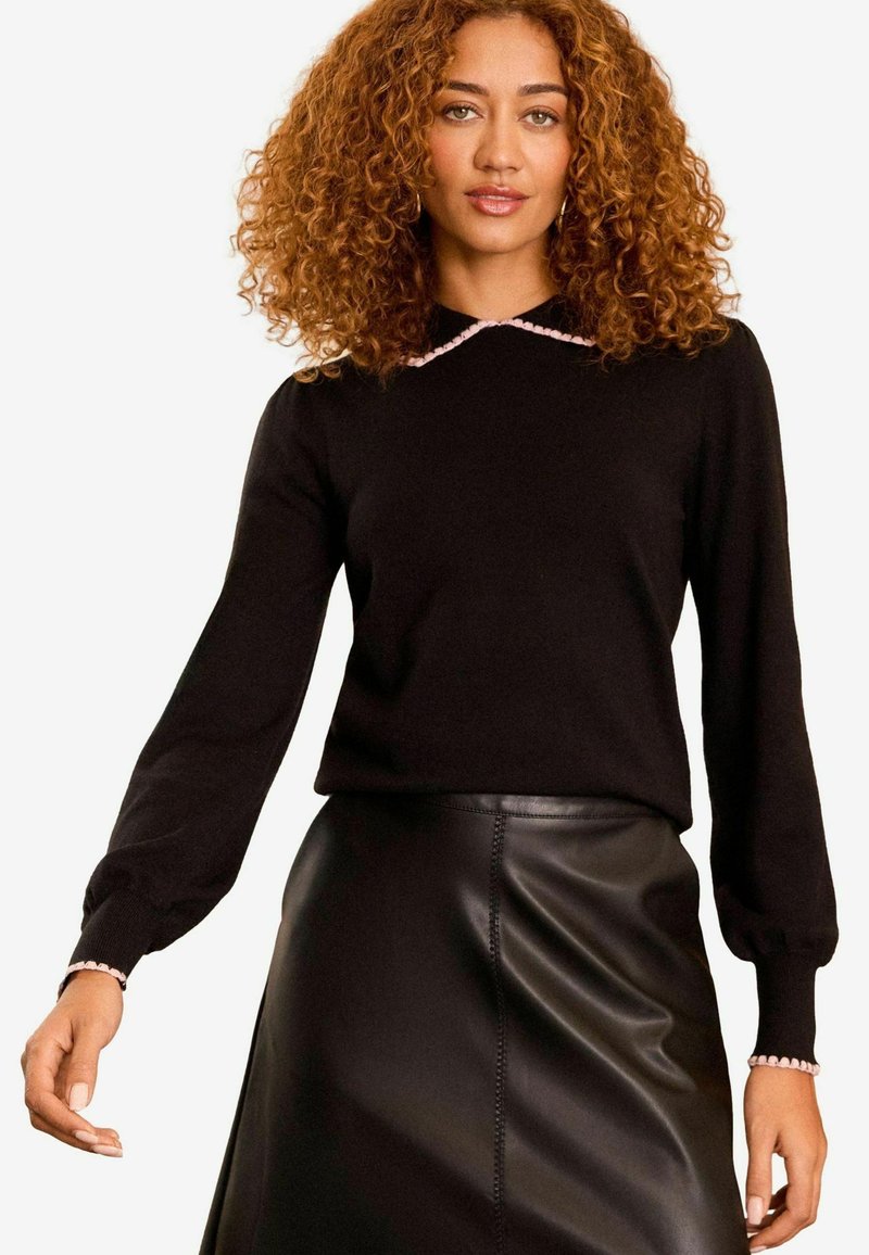 Svart tröja med lång ärm och rosa vågformad krage. Bärs tillsammans med en svart läderskjol, vilket framhäver en elegant silhuett.