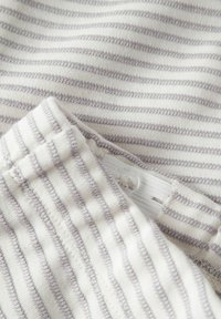 Tissu rayé blanc et gris avec un gros plan sur une ceinture dotée d'un bouton réglable et d'une bande élastique à l'intérieur.