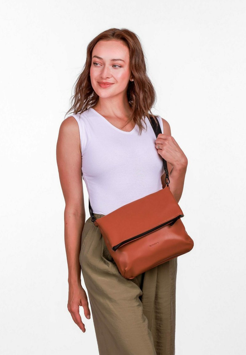 Braune Leder-Crossbody-Tasche mit einem umklappbaren Klappdeckel und Reißverschluss. Verfügt über einen schwarzen verstellbaren Gurt und eine glatte, matte Oberfläche.