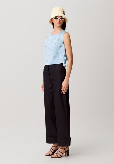 Top azzurro senza maniche con ricamo floreale, abbinato a pantaloni neri a gamba larga. Il look è completato da un cappello a secchiello bianco e sandali con tacco a listini.
