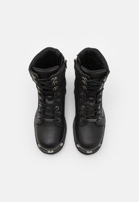 Botas de tobillo negras con un exterior de cuero liso, diseño con cordones, ojales metálicos y adornos de hardware plateado cerca de la punta.