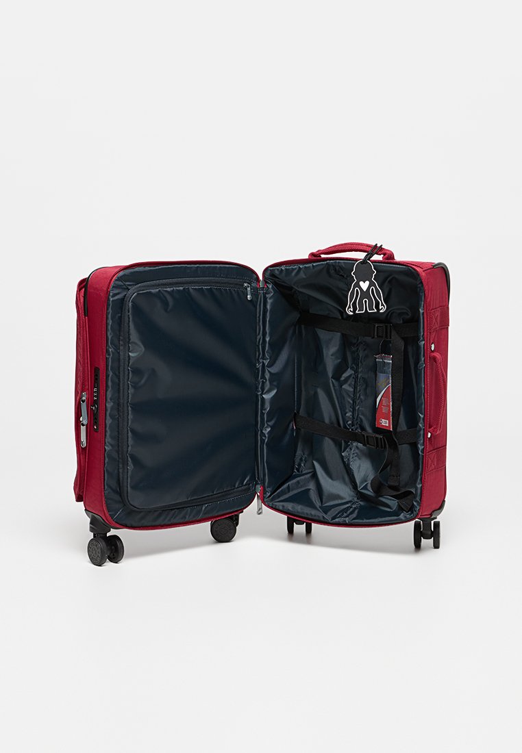 Roter Hartschalenkoffer mit blauer Innenausstattung, mit Reißverschlussfächern, verstellbaren Riemen und Rollen für Mobilität. Enthält ein Charm-Detail.