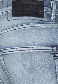 Vaaleansiniset farkut, joissa on musta nahkaleima, johon on embossattu "DIESEL", näkyvät saumat ja minimalistische takataskujen yksityiskohdat.