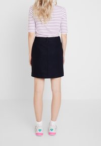 Marinblå kjol med skräddarsydd design, med en slits bak och ögla, parat med en randig, figurnära topp och vita sneakers med rosa detaljer.