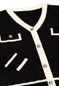 Schwarze Strickjacke mit cremefarbener Einfassung, ausgestattet mit einem V-Ausschnitt, zwei Fronttaschen und dekorativen Knöpfen mit einem kreisförmigen Design. Strickstoff mit Struktur.