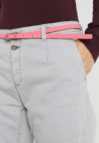 Szare spodnie z zapięciem na guziki posiadają jasno różowy pasek, który jest lekko fakturowany i oplata talię. Top jest w ciemnym bordowym kolorze.