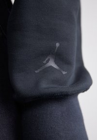 Dark navy sportswear fabric featuring a smooth texture and a subtle, reflective Jumpman logo on the sleeve. Close-up view focuses on detail.