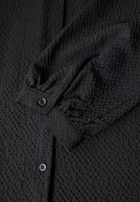 Camicia nera in tessuto testurizzato con un panno patterned, polsini con bottone e dettagli con maniche arricciate.