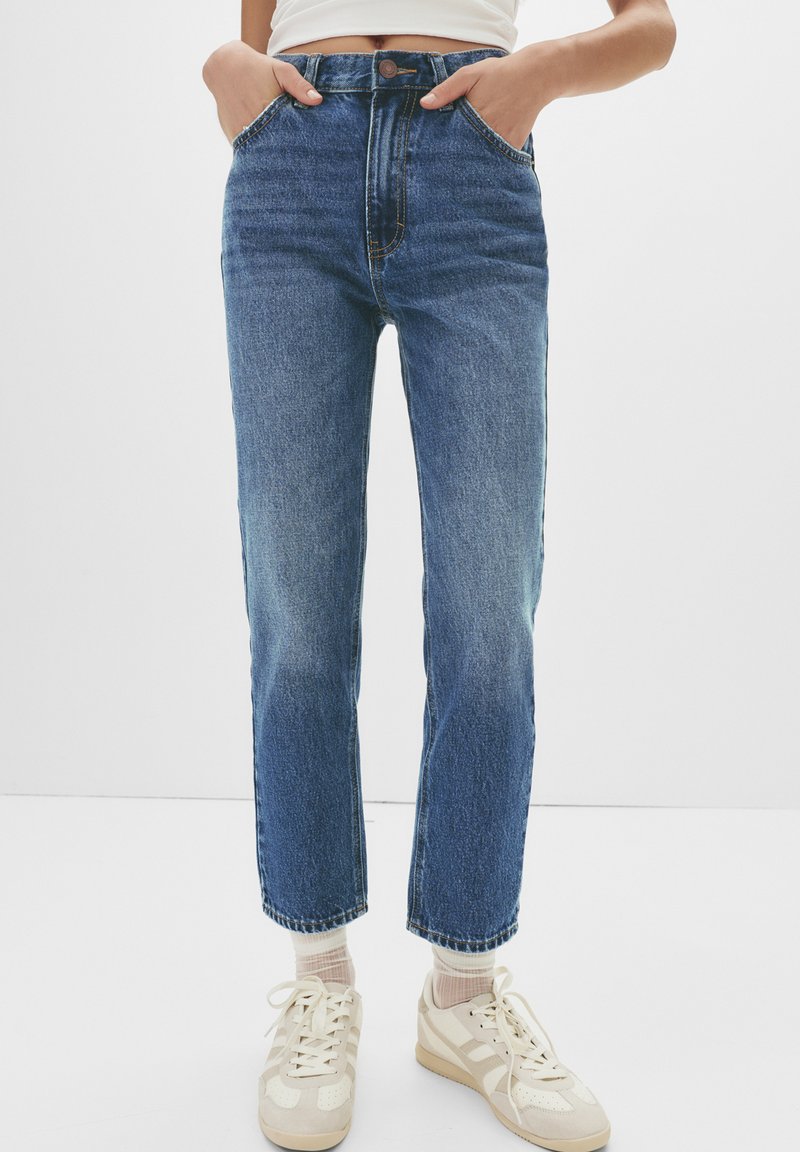 High-waisted blue denim jeans with a straight leg, featuring a button closure, front pockets, and subtle fading along the thighs.
