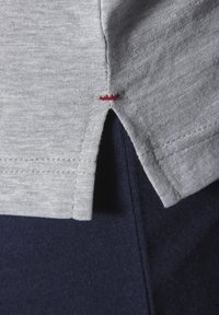 Gray cotton fabric with a split hem detail, featuring red stitching. Dark navy fabric is visible underneath, highlighting the layered design.