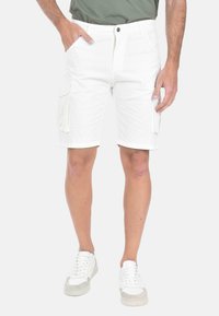 Pantaloni cargo bianchi realizzati in cotone, dotati di due tasche laterali, chiusura con bottone e orlo arrotolato. Abbinati a sneaker bianche.